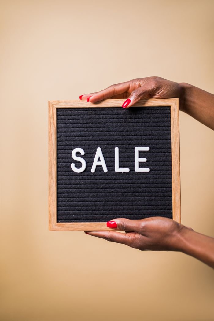 Close-up of hands holding a 'SALE' sign against a beige background, perfect for promotional use.